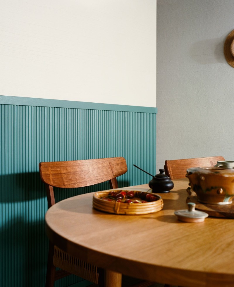 blueish green wall panel behind natural wooden dinner table set 