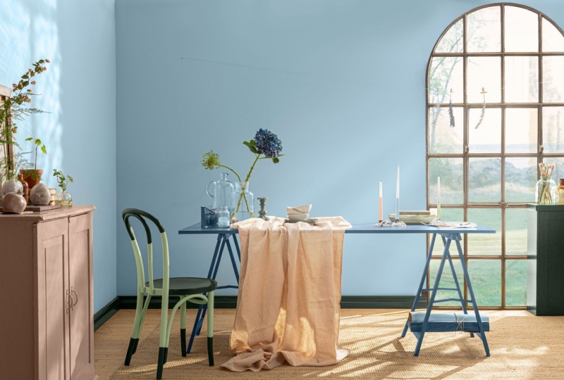 mėlynos spalvos siena ir žalios spalvos pietų stalas su kėdėmis
